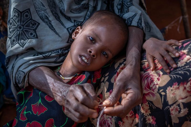 Un bambino rannicchiato sul grembo di una persona guarda dritto verso l'obiettivo, in una fotografia scattata con Canon EOS 5D Mark IV da Mulugeta Ayene.