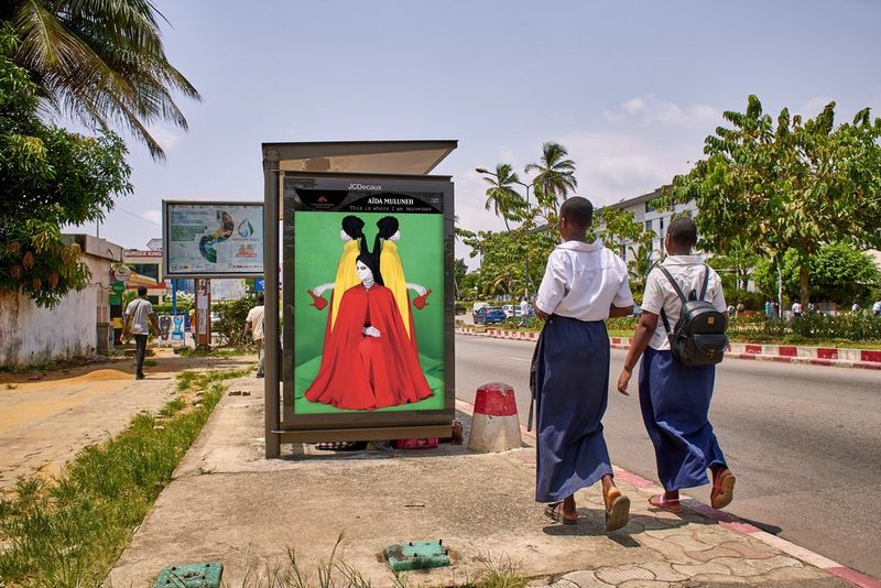 Two figures walk towards a bus stop displaying Aïda Muluneh's 2022 artwork To Speak In Silence.