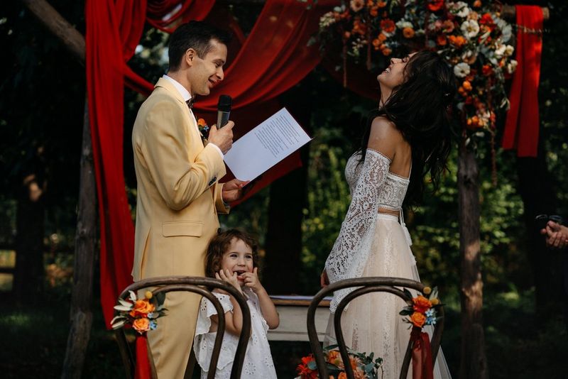 A groom reading his vows to his laughing bride, with a smiling young child leaning against his legs. Taken on a Canon EOS R3 by Canon Ambassador Adam Trzcionka.