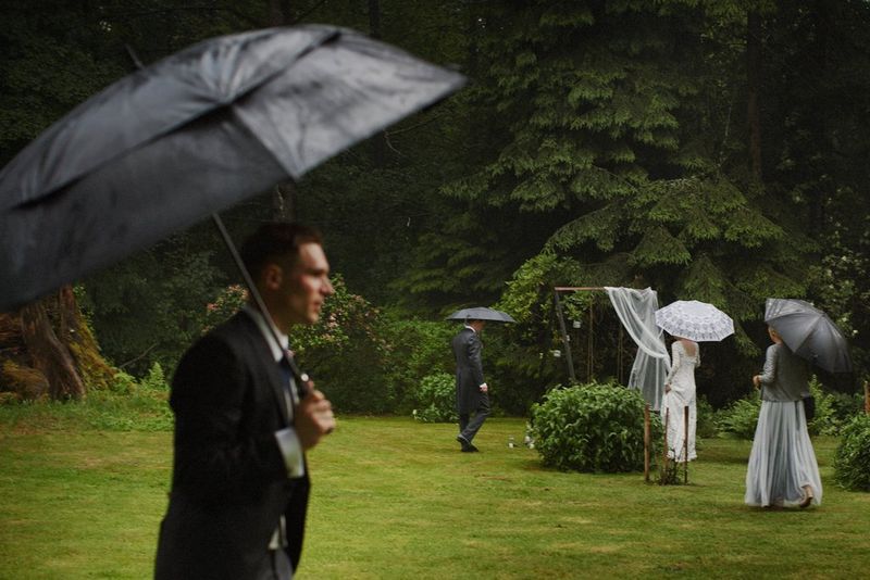 Members of a wedding party walking with umbrellas through a rain-drenched garden. Taken by Canon Ambassador Adam Trzcionka.