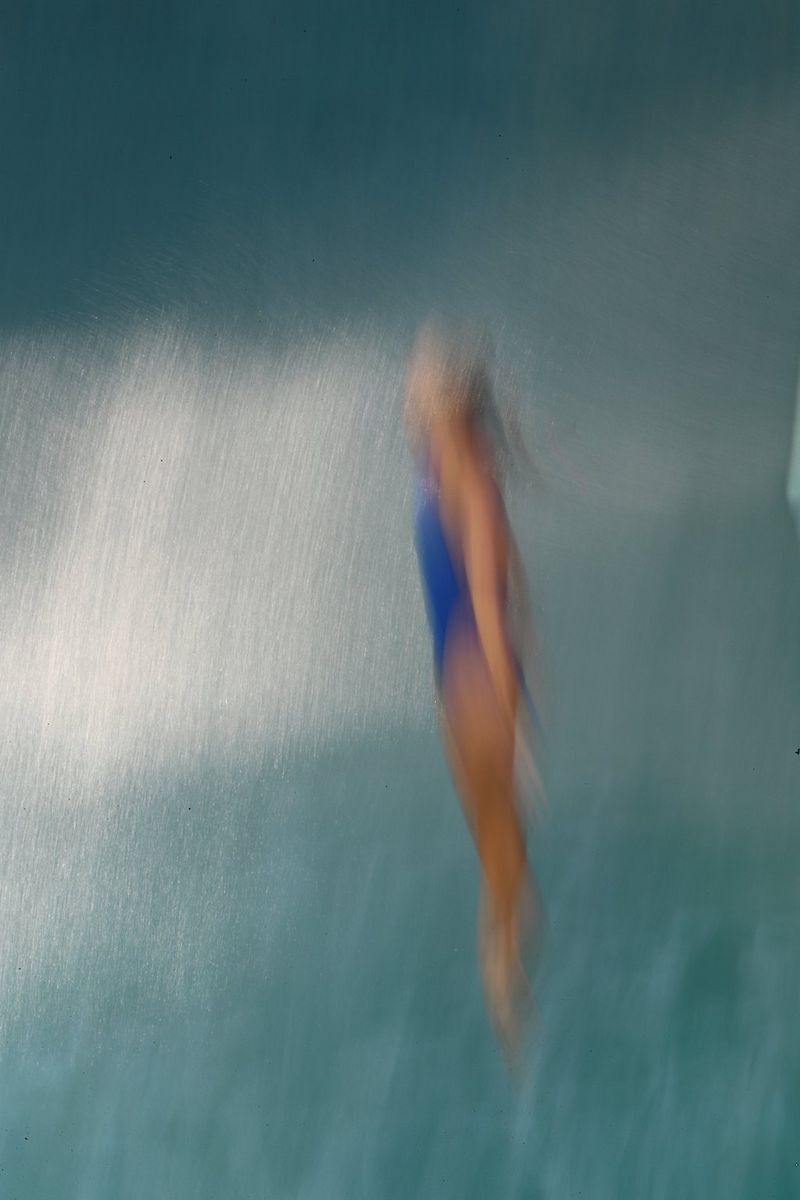 A blurred image of female diver in a blue swimsuit about to hit the water.