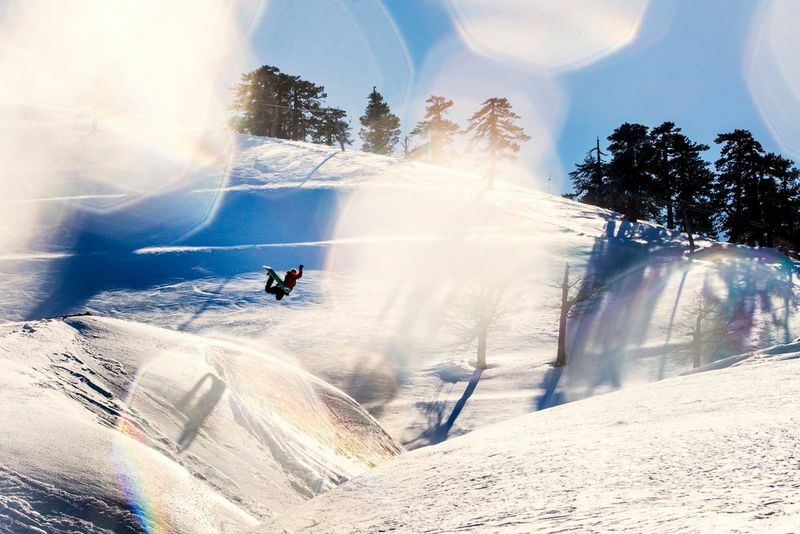 A person on a snowboard performs a stunt in a snowy landscape. The camera's lens is partially covered by snowflakes. Taken by Canon Ambassador Alexandros Grymanis. 