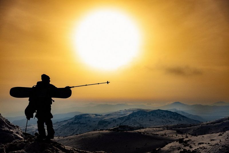 A person standing on a mountainside holding skis points his ski stick to the distance, silhouetted against the sun, in a photo taken on a Canon EOS R3 by Canon Ambassador Alexandros Grymanis.