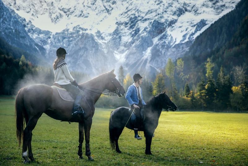 Two people on horses stand in a green landscape, trees and snow-capped mountains visible in the background. Taken on a Canon EOS-1D X by Canon Ambassador Aljoša Rebolj.
