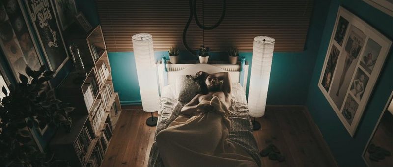A man lies on his back on a bed in the middle of a bedroom, one arm behind his head and another holding onto the blanket over his body, in a still from Uninhabitable shot by Canon Ambassador Burak Günaydın.