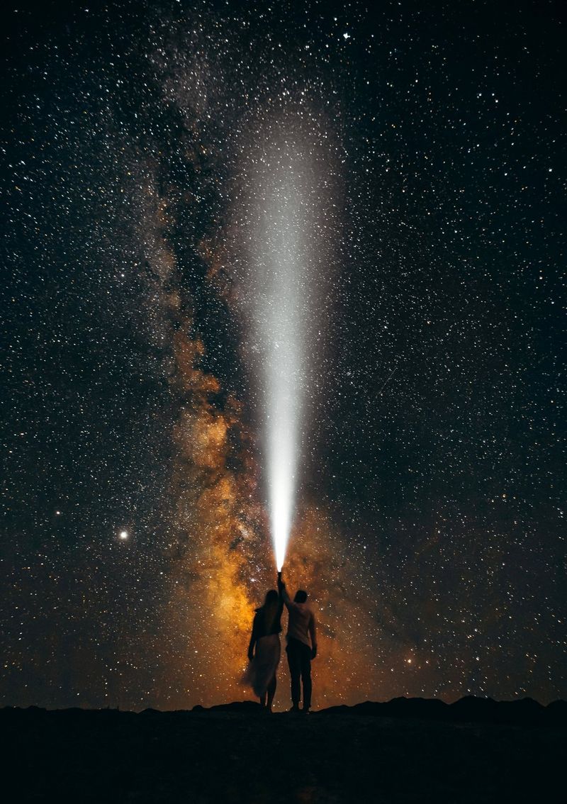Under a starry sky, a couple holds a flashlight, its beam pointing upwards. Taken on a Canon EOS 5D Mark IV by Canon Ambassador Askar Bumaga.
