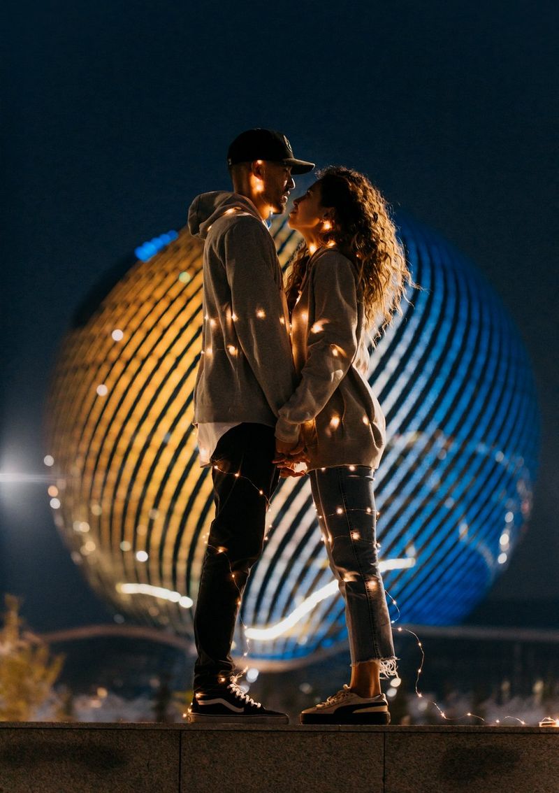  A couple wrapped up in fairy lights stands against a yellow and blue sphere. Taken on a Canon EOS 5D Mark IV by Canon Ambassador Askar Bumaga.