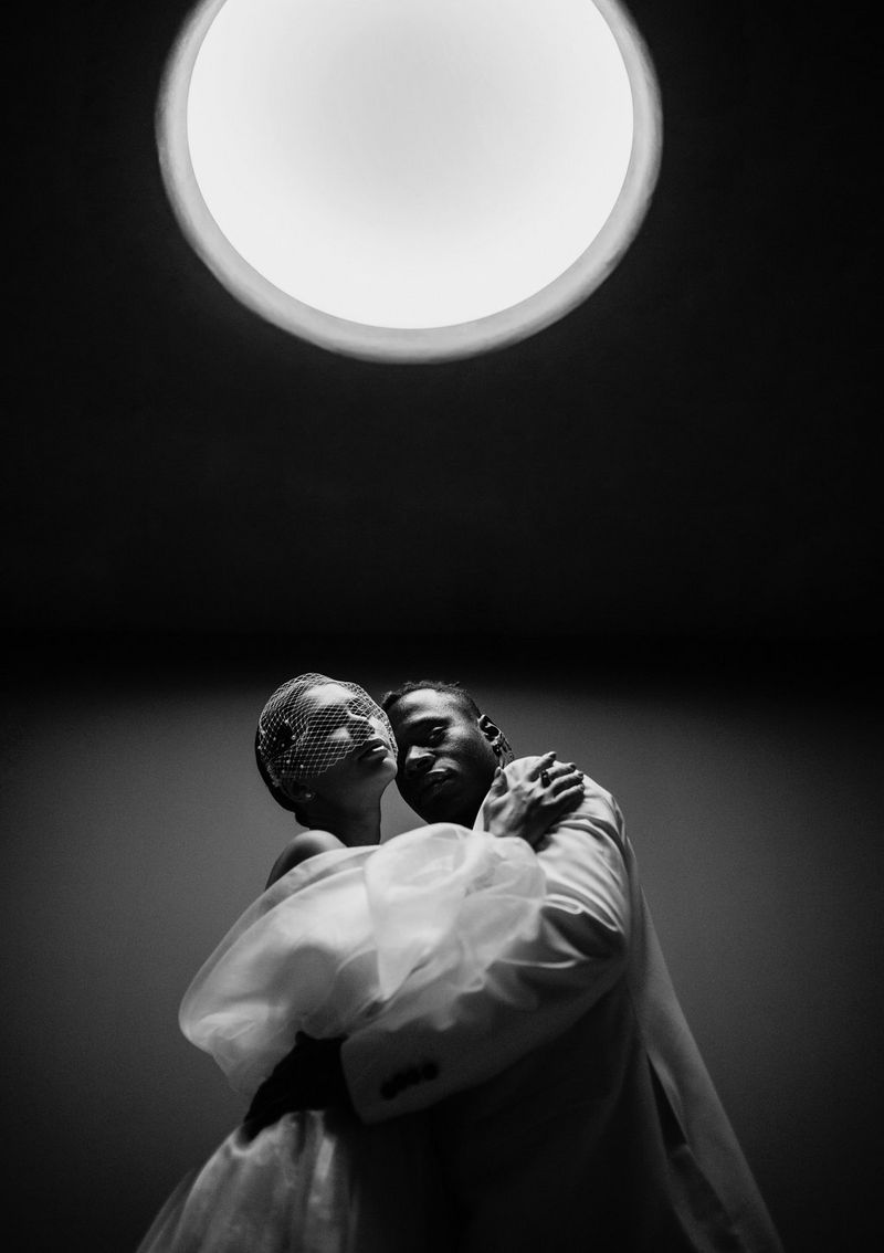 A black and white photo of a couple holding each other under a big white light. Taken from a low angle on a Canon EOS R6 by Canon Ambassador Askar Bumaga.