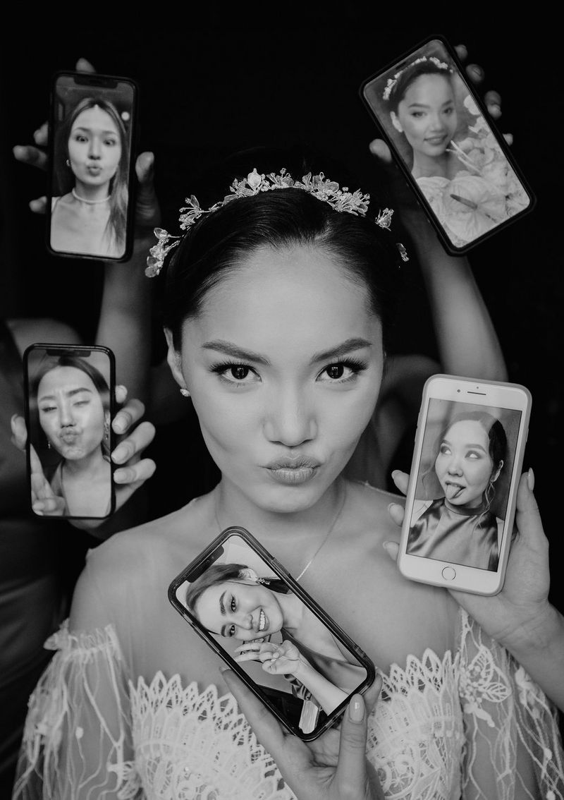 A black and white photo of a pouting bride, surrounded by hands holding smartphones showing different photos of her bridesmaids. Taken on a Canon EOS R6 by Canon Ambassador Askar Bumaga.