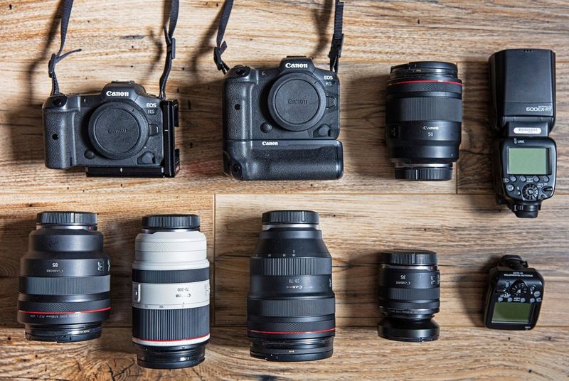 Een foto van een Canon-uitrusting die netjes is gerangschikt op een houten vloer, bestaande uit twee camera's, vijf objectieven, en flitsverlengstukken.