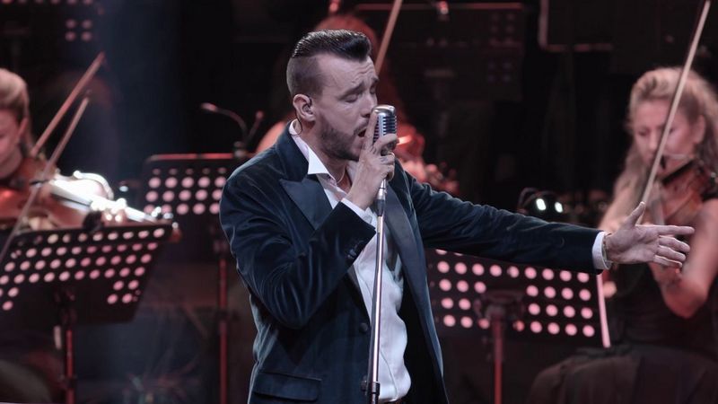Turkish musician Cem Adrian sings into a microphone on stage, violinists behind him, in a still from Canon Ambassador Burak Günaydın's showreel.