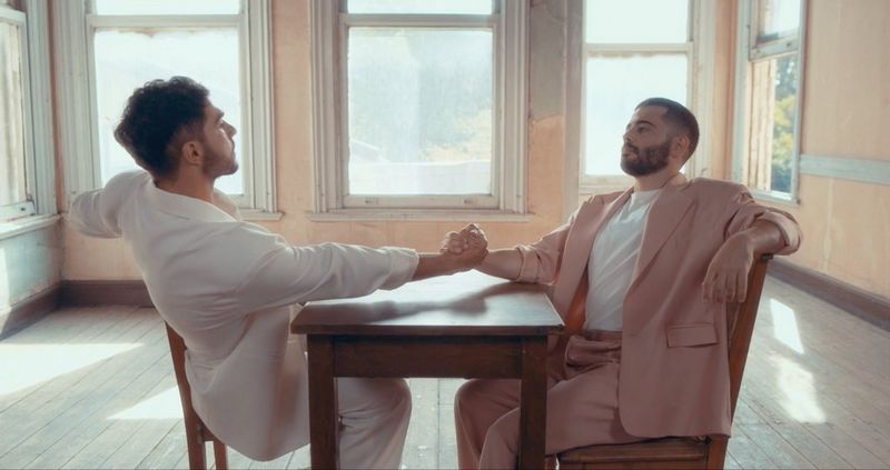 A still from the music video for Hakan Kalgıdım's song Dökünce Gül Dikenlerini, showing two men in suits appearing to arm wrestle in an empty room. Shot on a Canon EOS C500 Mark II by Canon Ambassador Çağla Çağlar.