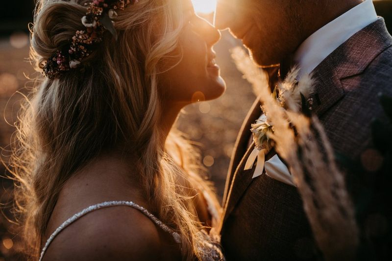 A close-up of a bride and groom gazing into each other's eyes, backlit by the setting sun.