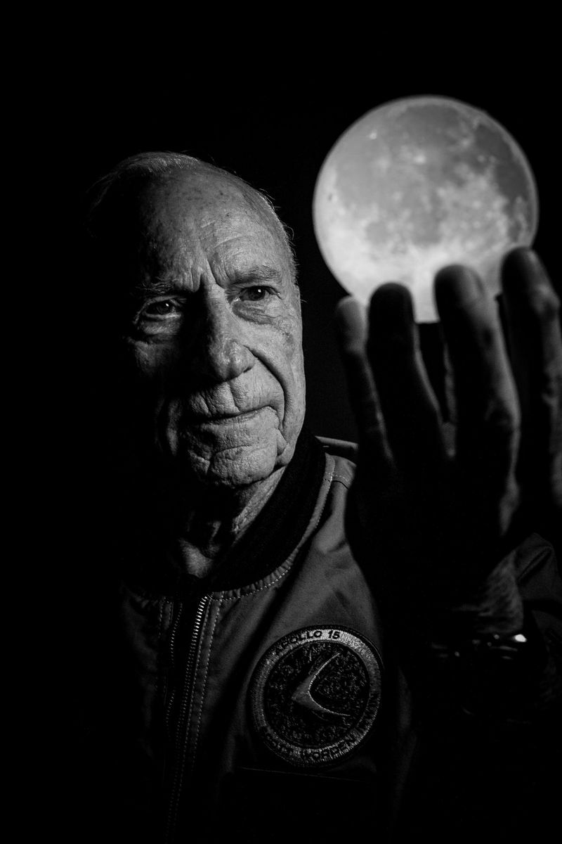 A black and white portrait of an elderly man holding a moon-shaped orb in front of his face.