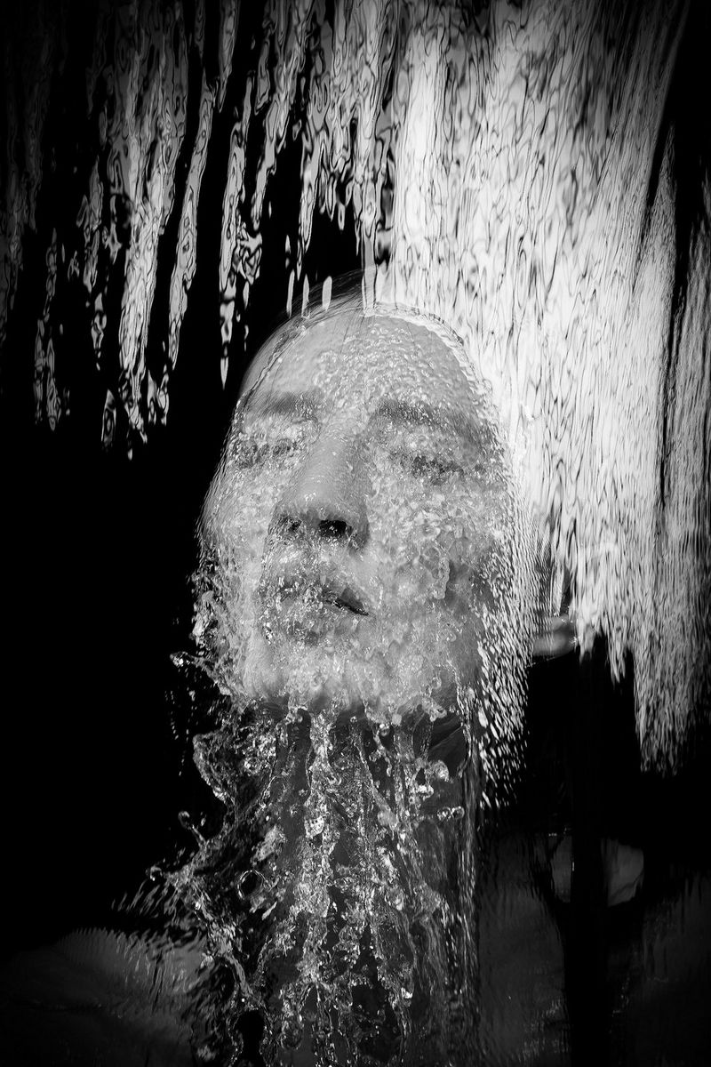 A black and white image of water cascading over a woman's upwards tilted face.