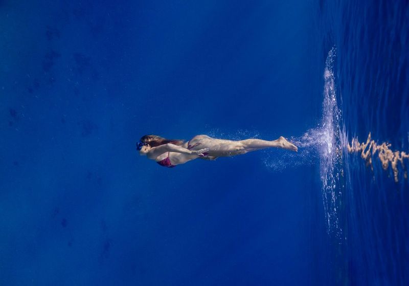 A female freediver is photographed underwater with bubbles in her wake after plunging into the sea. 