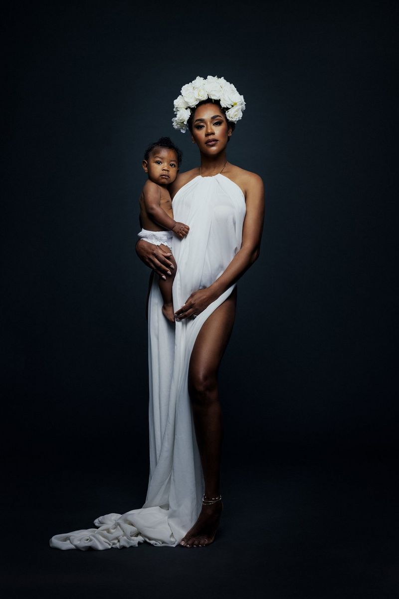 A portrait of a woman, wearing a long white dress and white floral headdress and holding a baby on her hip, taken on a Canon EOS R5 with a Canon RF 28-70mm F2L USM lens by Donatella Nicolini.