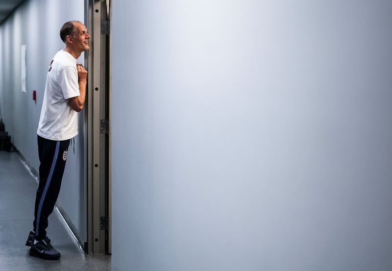 A smiling man in sports gear leaning against a door frame. The figure is in the first third of the frame, while the rest of the image is made up a blank wall.