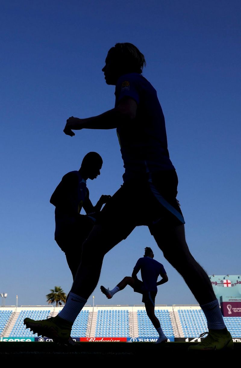 England football players silhouetted against a bright blue sky during a training session.