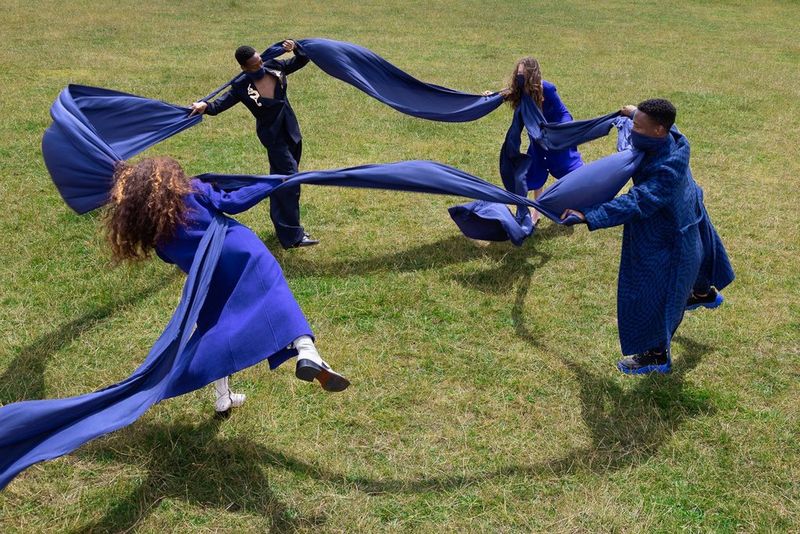 A circle of dancers connected by a long blue silk scarf which is wrapped around their faces.
