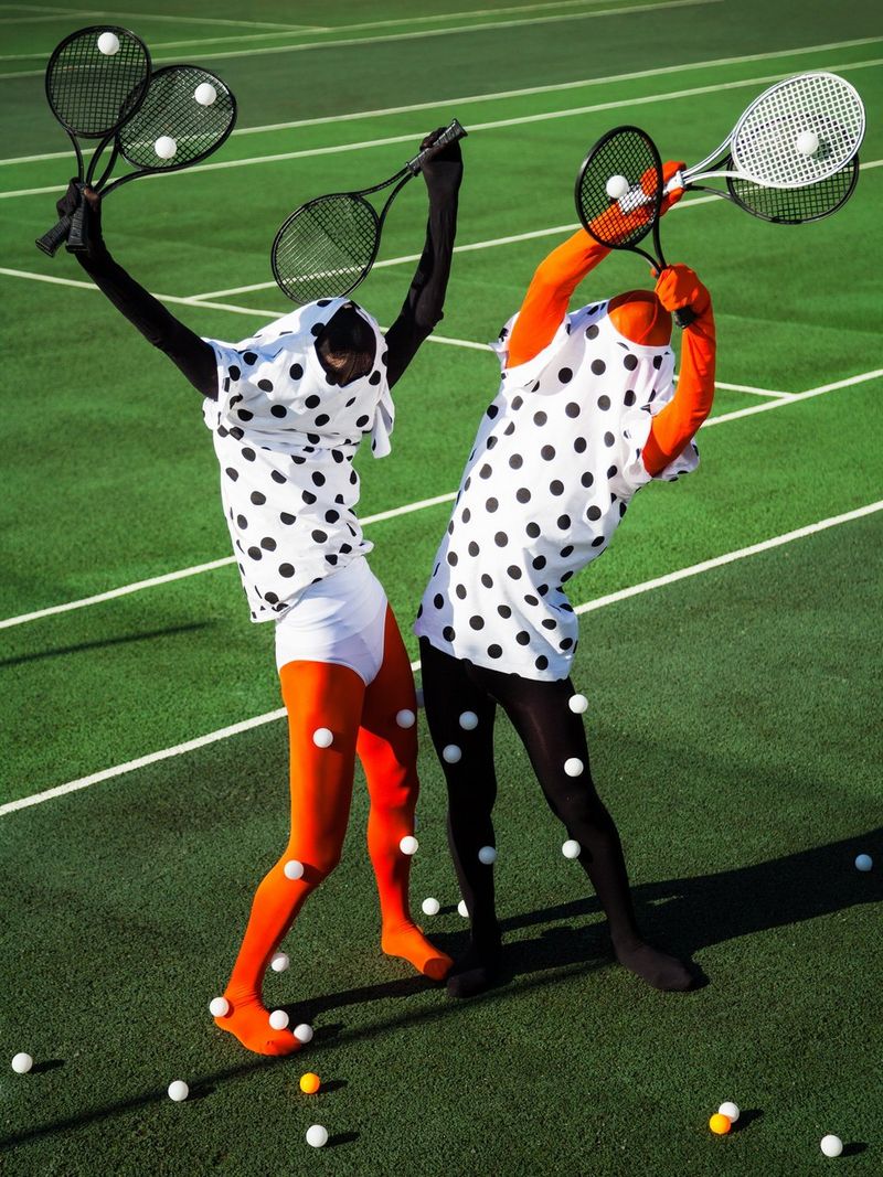 Two models in tights and polka dot tops and with their faces obscured hold tennis rackets in the air. 