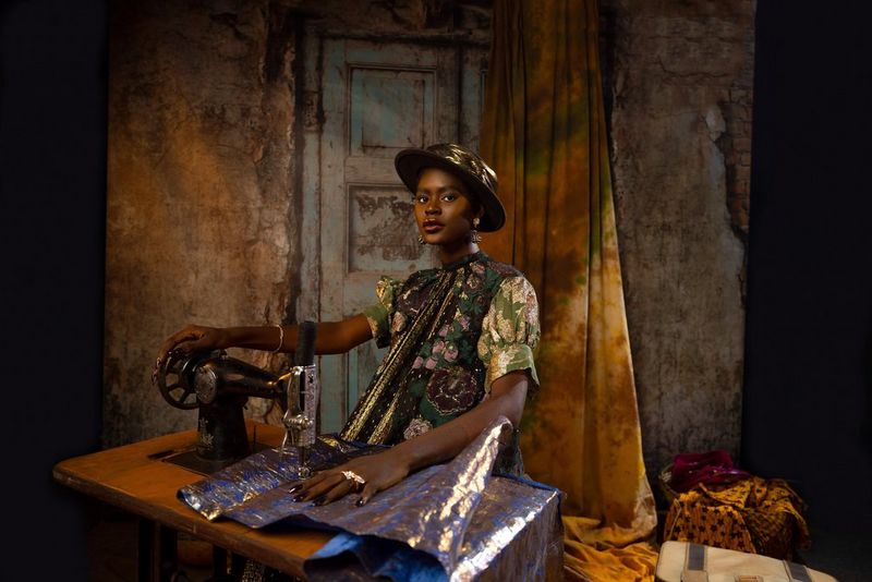 Une femme vêtue d'un chapeau et d'une robe brodés, en train d'utiliser une machine à coudre ancienne.