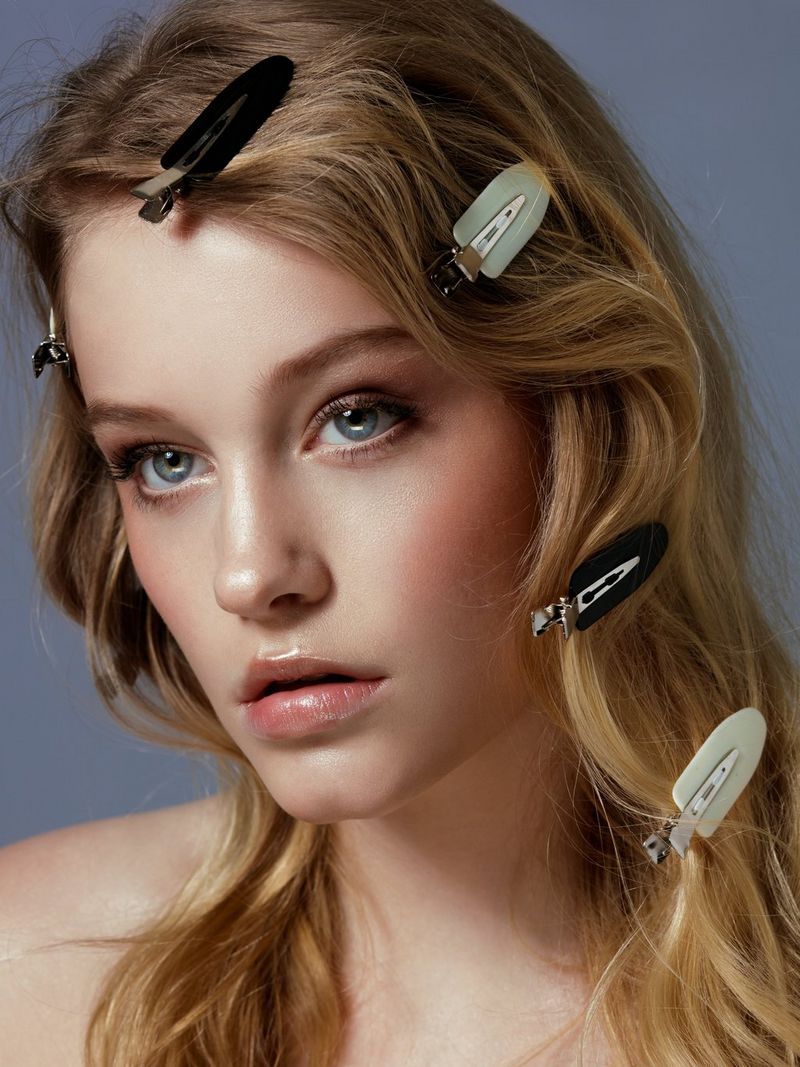 A close-up of a model with long, wavy hair fixed with different styles of hair clips.  
