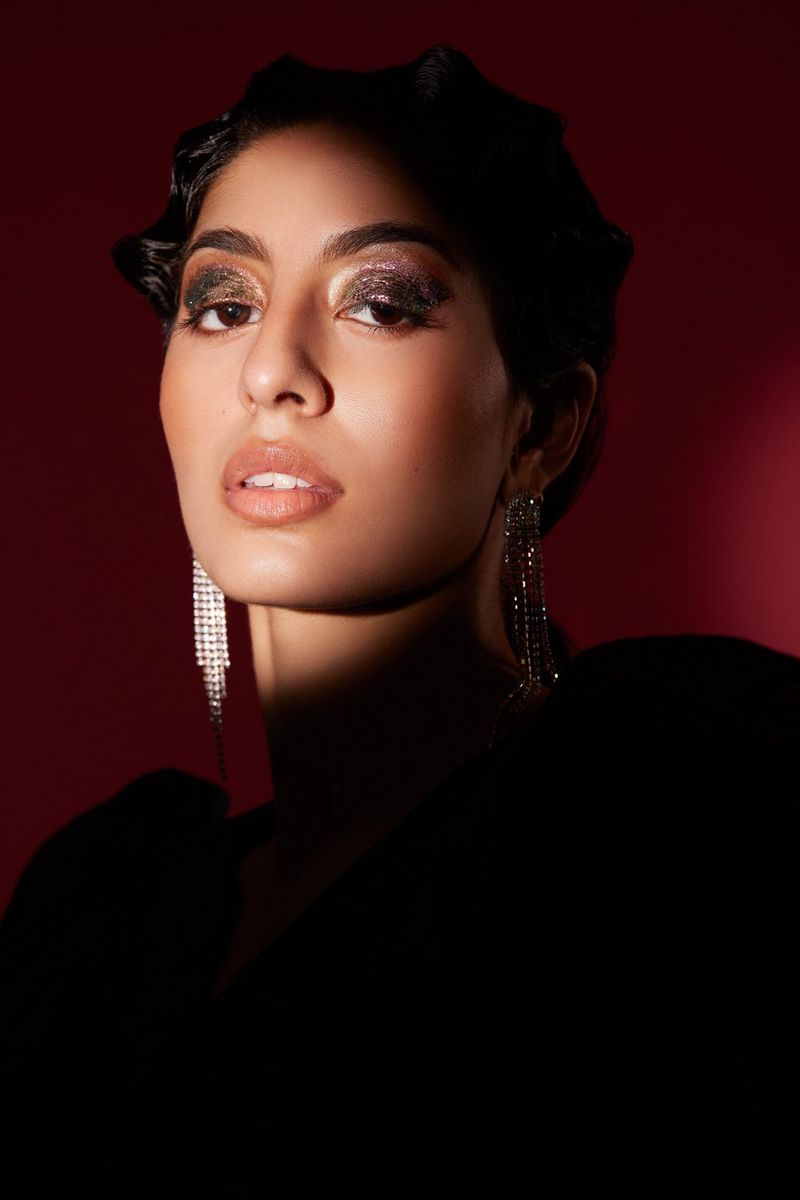 A portrait of a model, lit from the side, wearing heavy eye make-up and long diamante earrings.