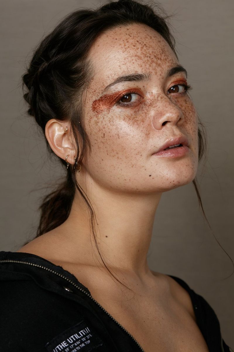 A side profile of a freckled model wearing shimmery bronze eyeshadow that extends from her eyelid across the side of her face. 