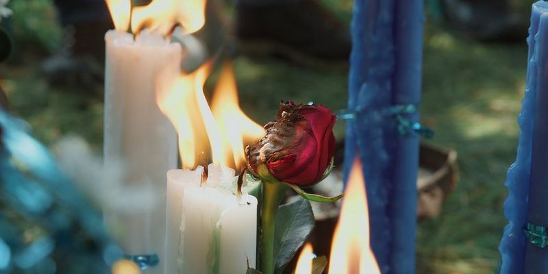 The petals of a red rose wither in the flames of slender white candles. Still from Barrio Bravo by Filippo Tommasoli.