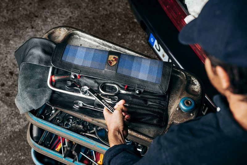 Shot from behind, a mechanic lifts a Porsche-branded wrench from his toolbox, taken on a Canon EOS R5 by Florian Roser. 