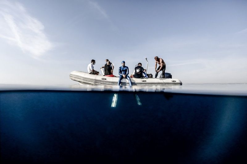 Un plongeur et son équipe se préparant sur une embarcation. L'appareil photo est à moitié submergé, laissant voir les palmes du plongeur sous la surface.