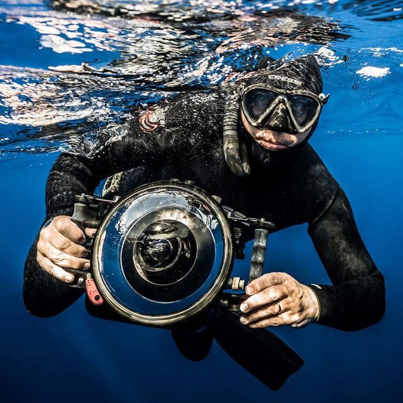 Canon Ambassador Franck Seguin holds a Canon camera in an underwater housing while diving just below the water's surface.