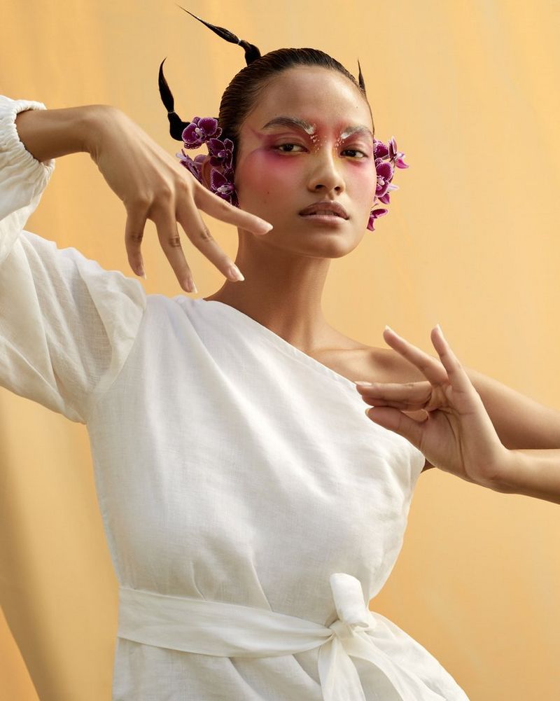 A model, in a white, belted one-shoulder dress, strikes a pose inspired by traditional Indian dance in a portrait by Canon Ambassador Heidi Rondak.
