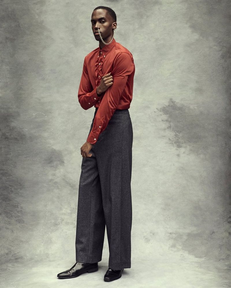 A full-length portrait of a model, posing against a grey backdrop in a red satin shirt and dark trousers, and with a chain hanging from his nose to his ear, by Canon Ambassador Heidi Rondak.