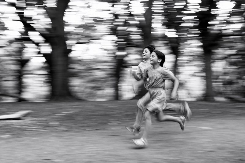 A black and white portrait of two girls running, shot with a panning technique to convey a sense of movement and speed.