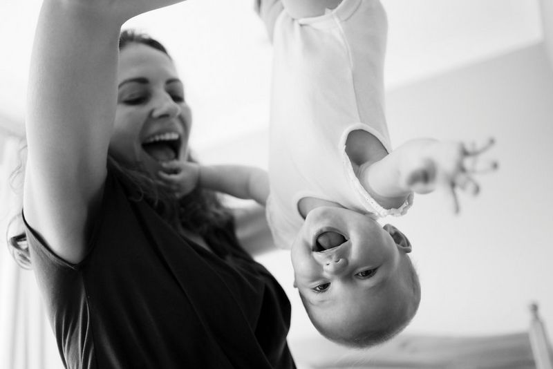 A black and white image of a smiling woman holding a laughing baby upside down.