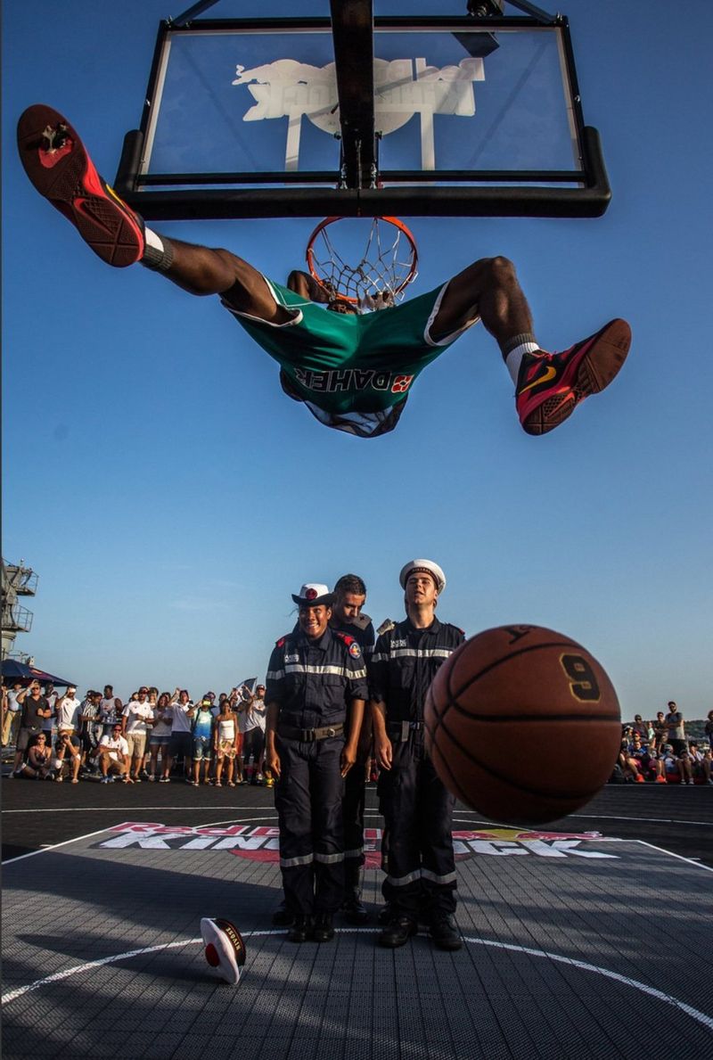 Un basketteur suspendu au panier après avoir marqué un dunk, sous le regard de membres de la Marine nationale française sur le pont d'un porte-hélicoptères.