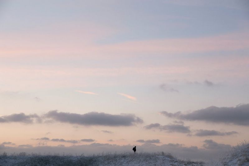 The silhouette of a person is visible under a cloudy sky. The sky appears to be different shades of pastel pink and pastel blue. Taken by Iiris Sjöblad. 