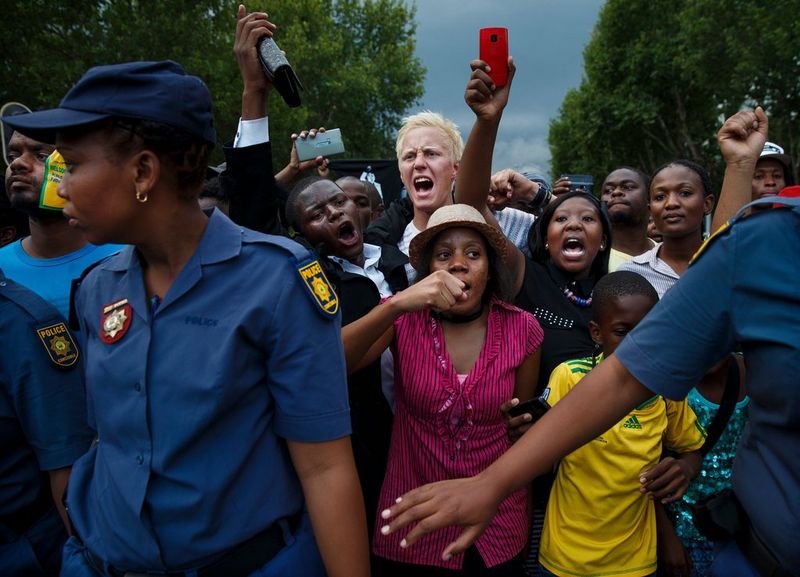South African police hold back a crowd of shouting people.