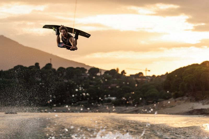 A wakeboarder performs an aerial manoeuvre, the warm evening light defining his silhouette against the sky.