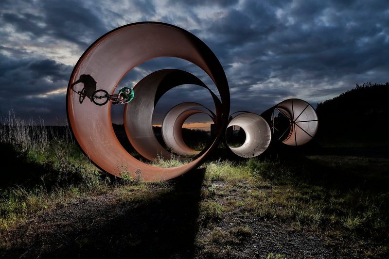 A BMX rider performing a stunt inside a large metal tube under darkened skies.