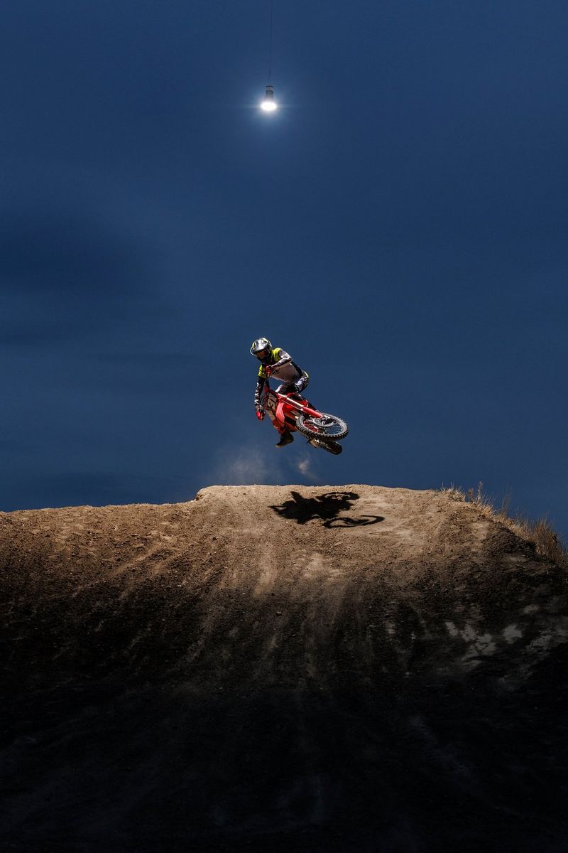 A motocross rider in mid-air, between the illuminated landscape below and the deep-blue sky above.