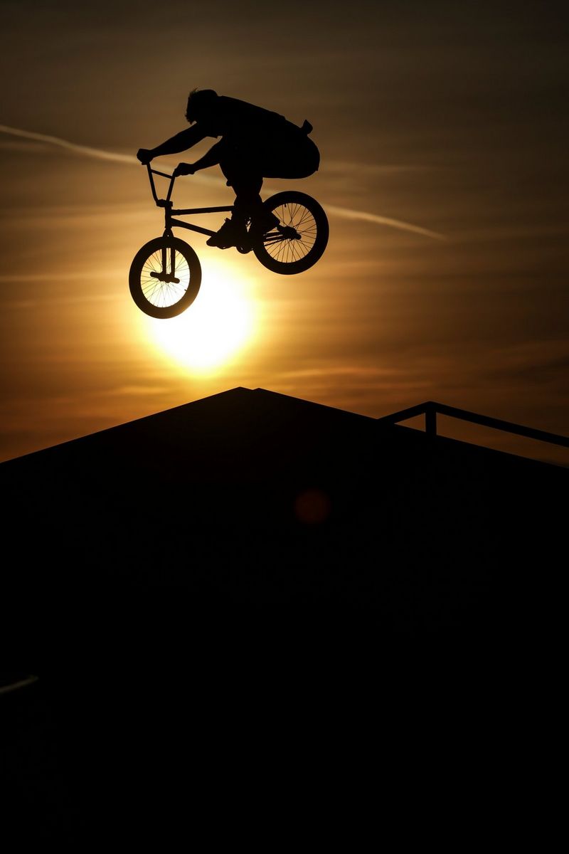A BMX rider crossing the setting sun at the peak of a jump, silhouetted against the evening sky.