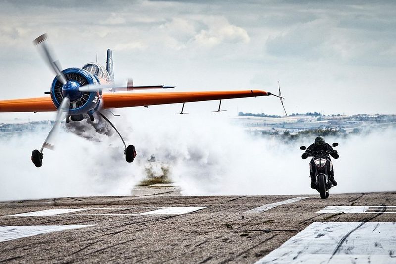 A stunt plane and a motorbike race towards the camera on a runway in Casarrubios, Spain.