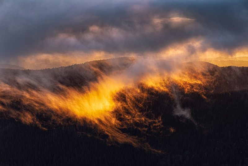 Low clouds drifting across a mountain ridge, backlit by the setting sun.