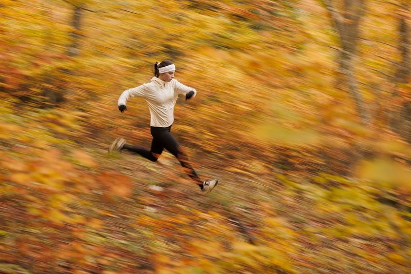 A female runner in cream jacket and black leggings racing through an autumnal landscape which has been blurred by the long exposure.