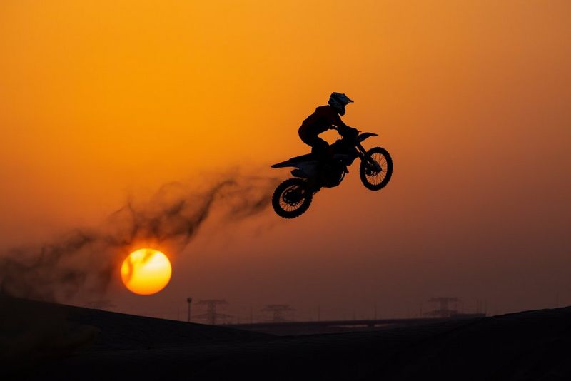 A silhouette of a motorbike rider performing a jump at sunset.