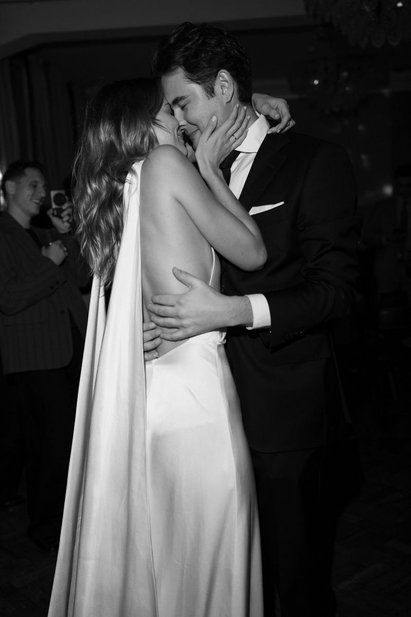 A bride and groom embrace on the dancefloor, the bride wearing a backless silky dress with a long train.