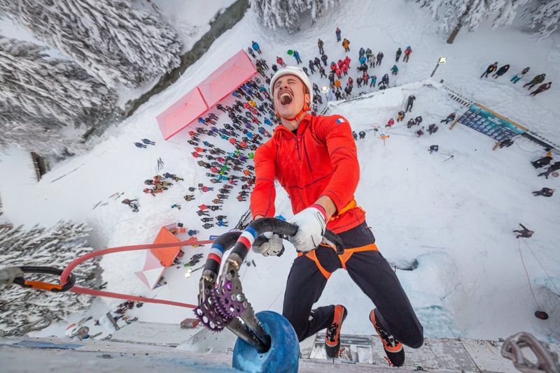 A climber celebrates their win, hanging from an ice wall far above the crowds on a snow-covered mountainside. Taken by Canon Ambassador Julia Roger-Veyer.